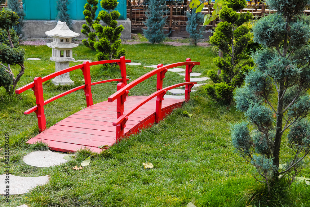 Beautiful city park with green lawn and red bridge