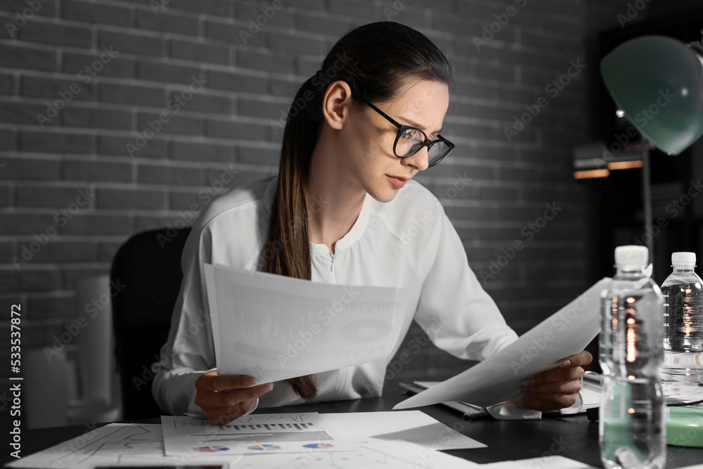 Beautiful businesswoman working with documents in office at night