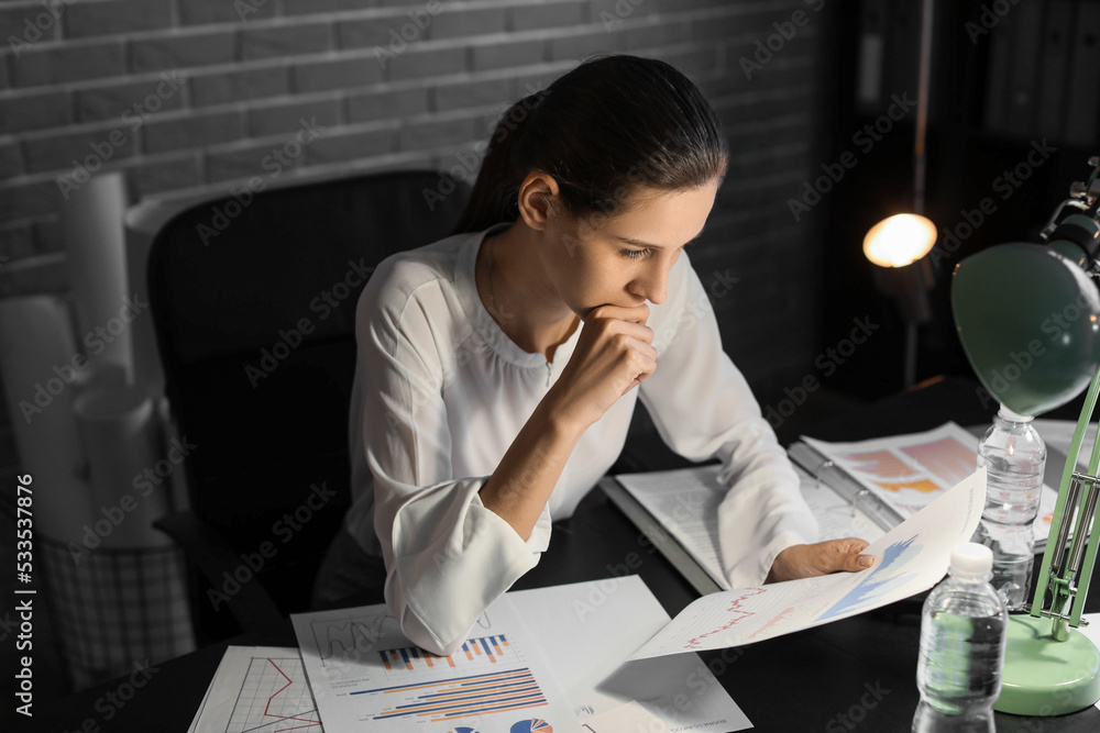 Beautiful businesswoman working with documents in office at night