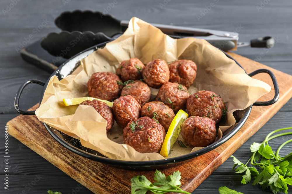 Board with baking dish, meat balls, paper and herbs on dark wooden background