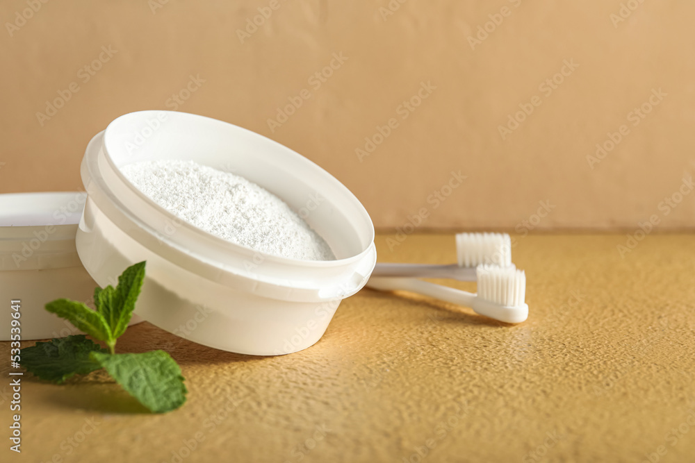 Jars of tooth powder with brushes and mint on beige background, closeup