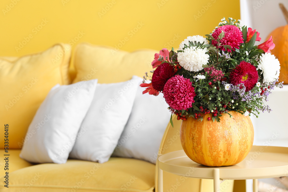 Pumpkin with beautiful flowers on table in living room, closeup