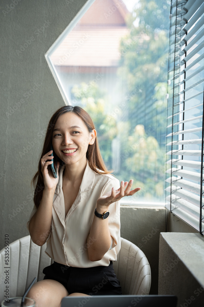 穿着正式西装的亚洲女商人在办公室里，在使用智能手机和工作时心情愉快。