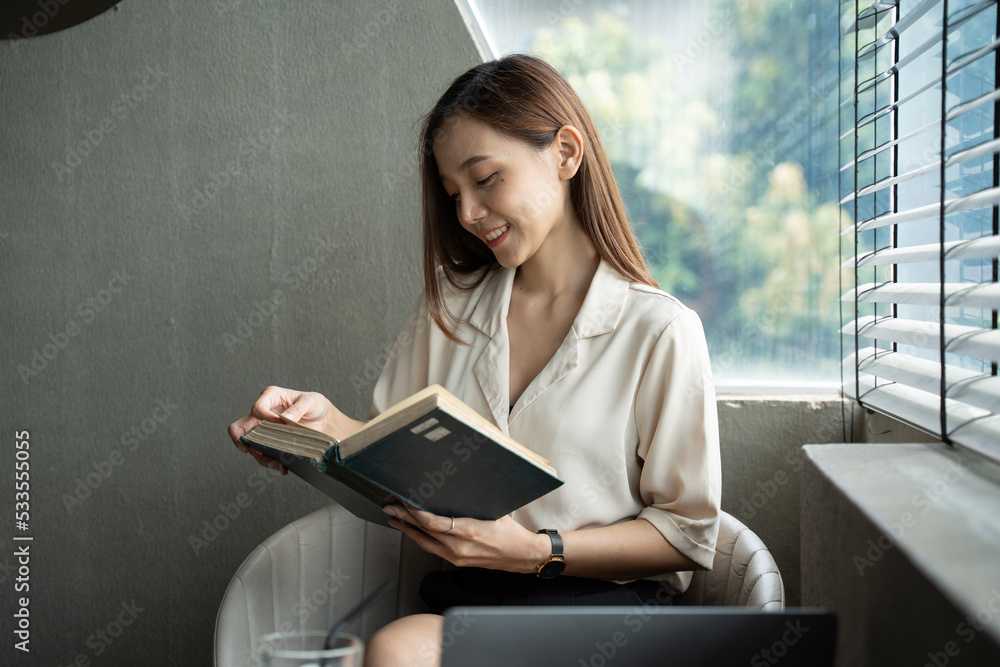 Young pretty woman sitting at opened window drinking coffee and reading a book enjoys of rest