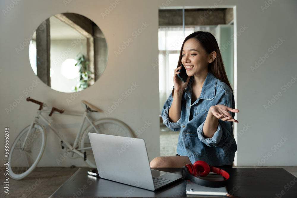 年轻的亚洲女人在咖啡店打电话，开心地笑着。