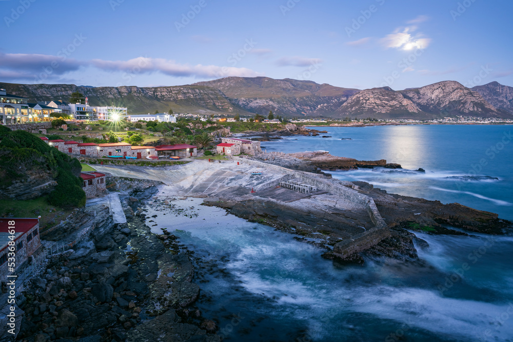 Evening view of Hermanus coastline, the Old Harbour in the foreground, the full moon rising above th