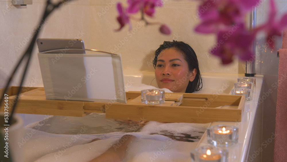 CLOSE UP: Relaxed young woman lying in bubble bath and watching an online movie