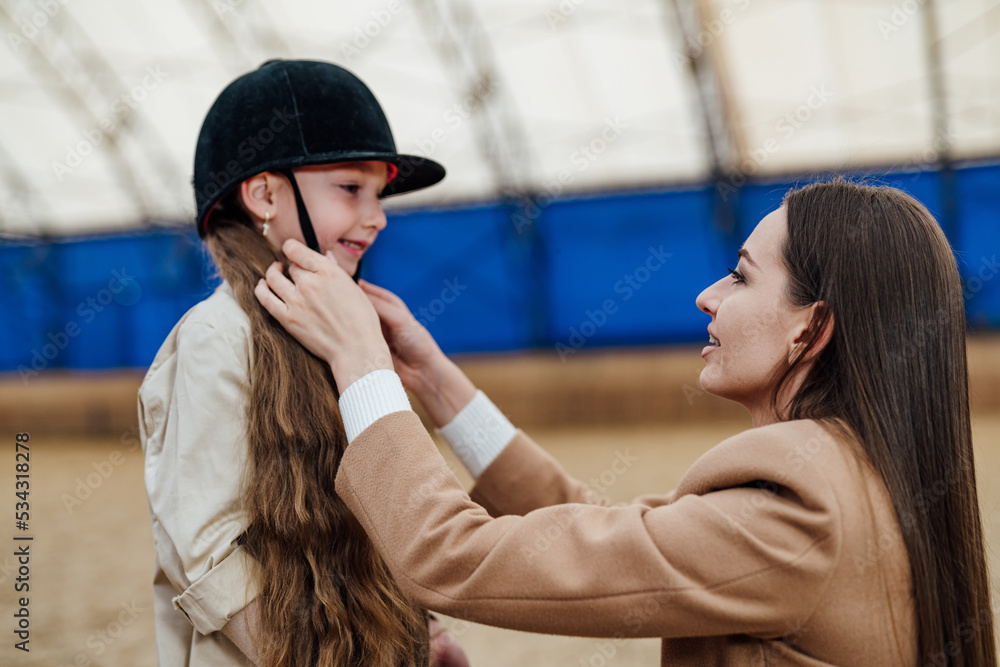 Young girl horse ride training. Pretty woman prepairing kid for horse riding.