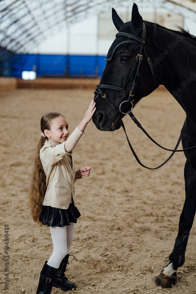 Little girl on countryside horse farm. Cute pretty girl in helmet jockey.