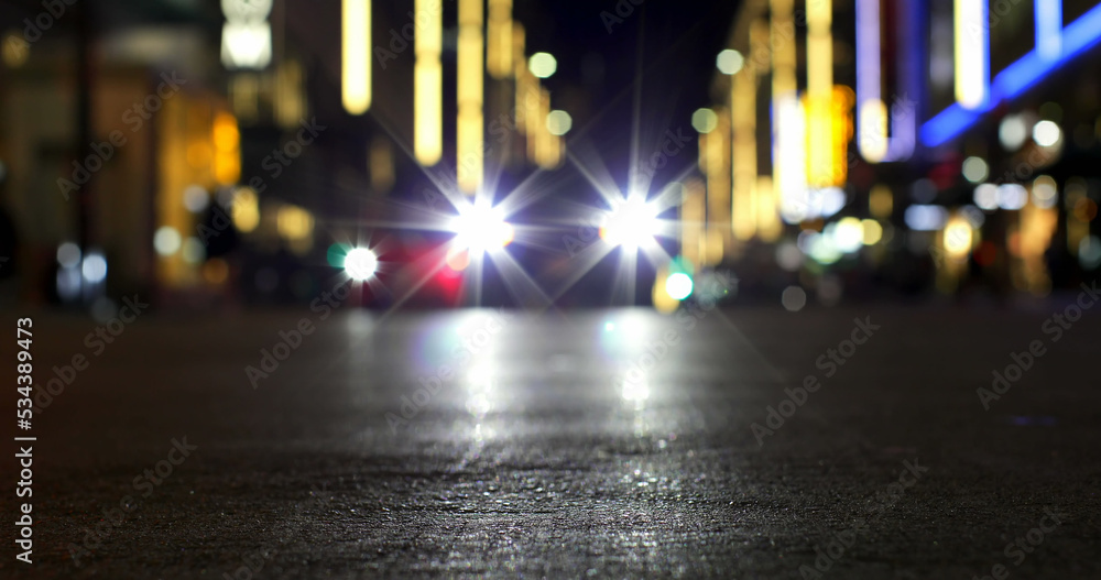 夜晚城市道路上，商店和路灯散焦，汽车前灯闪闪发光的图像