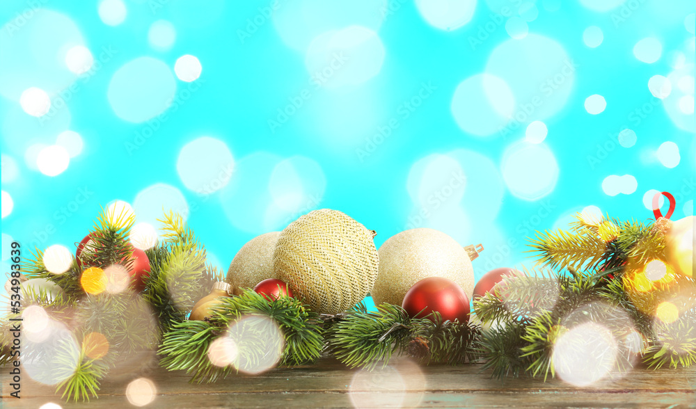 Christmas balls and fir branches on wooden table against light blue background