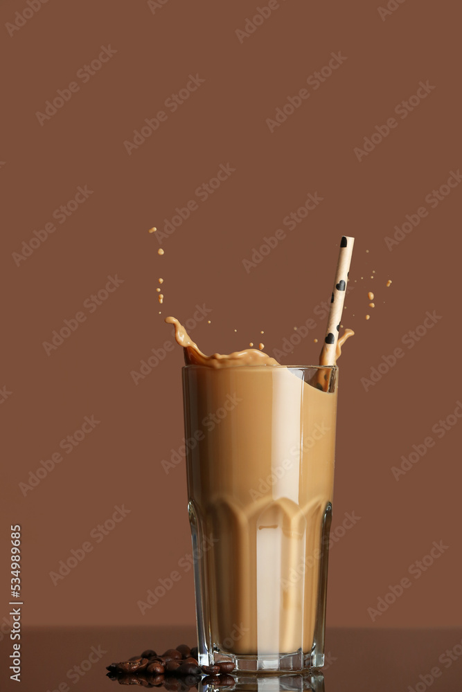 Glass of tasty iced coffee with splashes and beans on color background