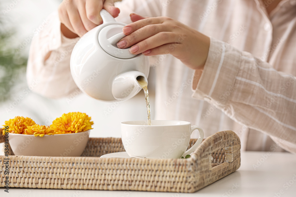 Woman pouring hot tea into cup at table in cafe