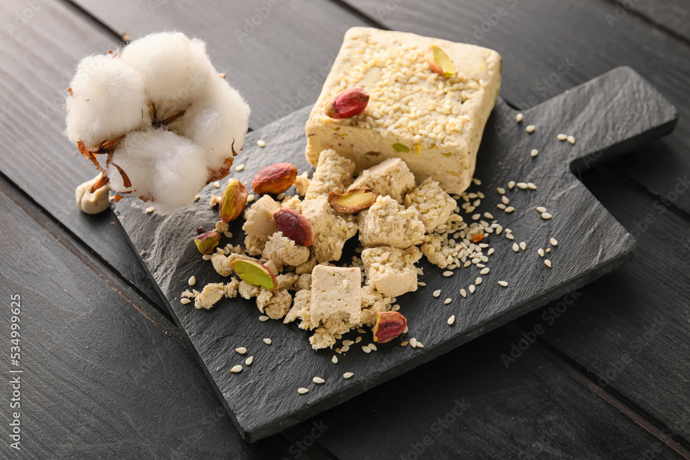 Board of sweet sesame halva with pistachios and cotton flower on dark wooden background