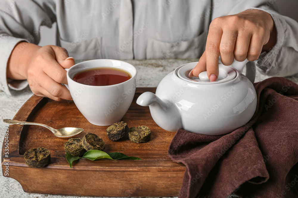 桌上放着一杯普洱茶、茶壶和干压叶的女性手，特写