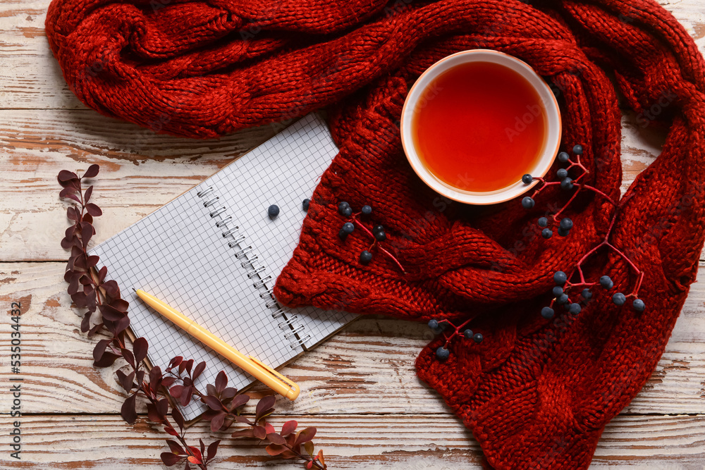 Opened notebook, cup of tea, knitted scarf and autumn decor on light wooden background