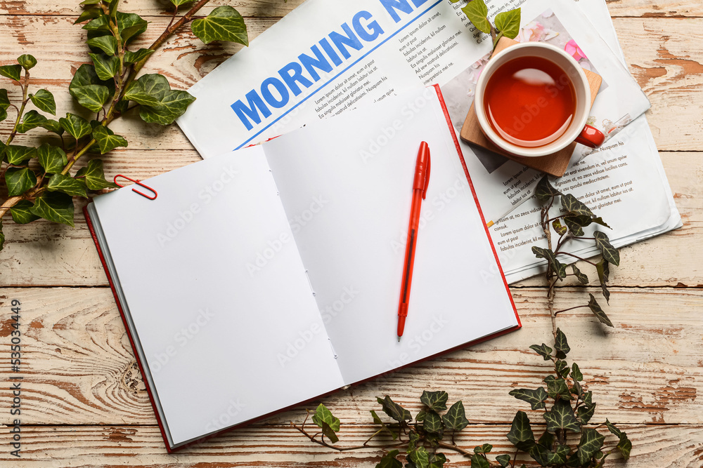 Opened notebook, newspaper, cup of tea and branches on light wooden background