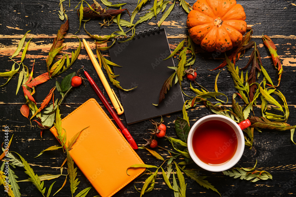 Notebooks, cup of tea, pumpkin and autumn decor on dark wooden background