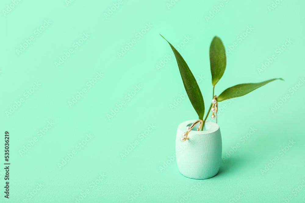 Showcase pedestal, earrings and floral decor on green background