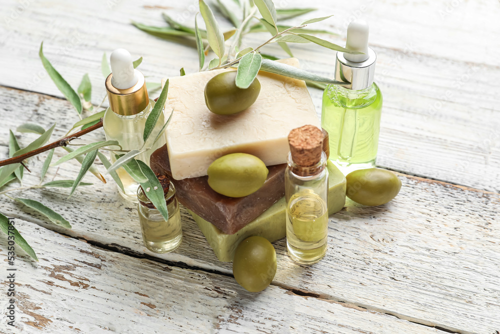 Bottles of olive essential oil and soap bars on light wooden background