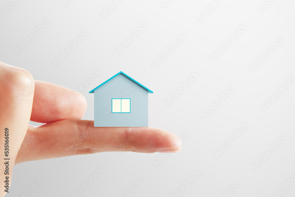 Mortgage and bank loan concept with small blue house layout on human finger on light background