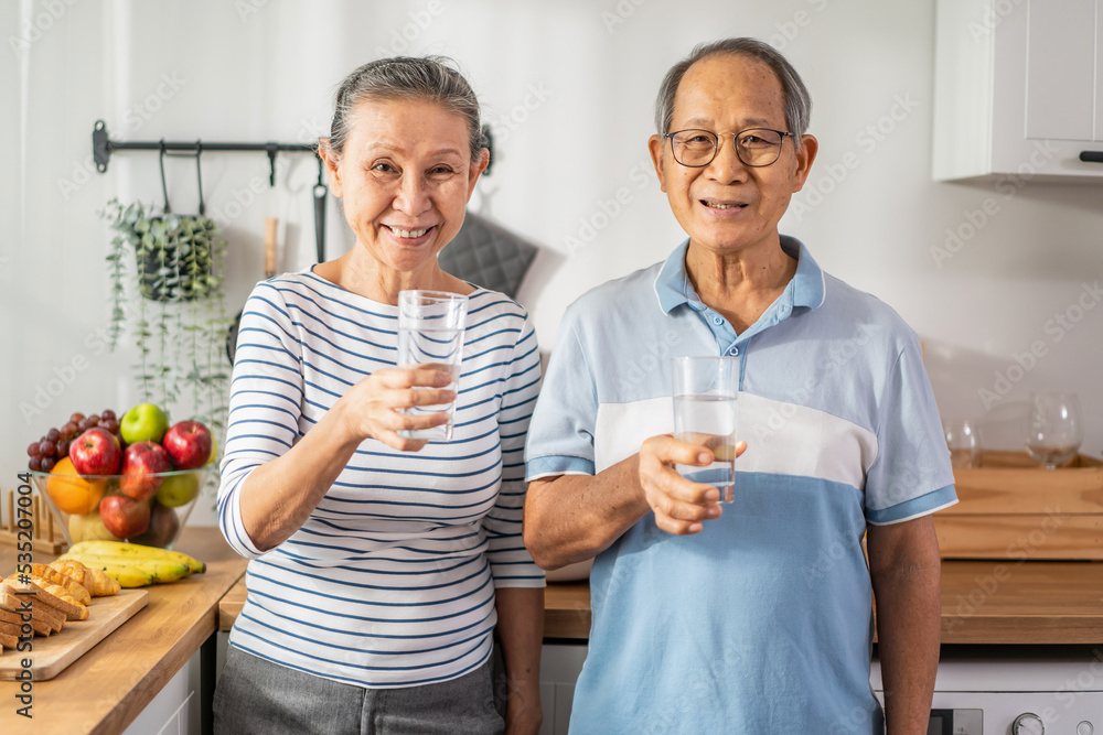 Portrait of Asian senior older couple drink glass of water in kitchen. 