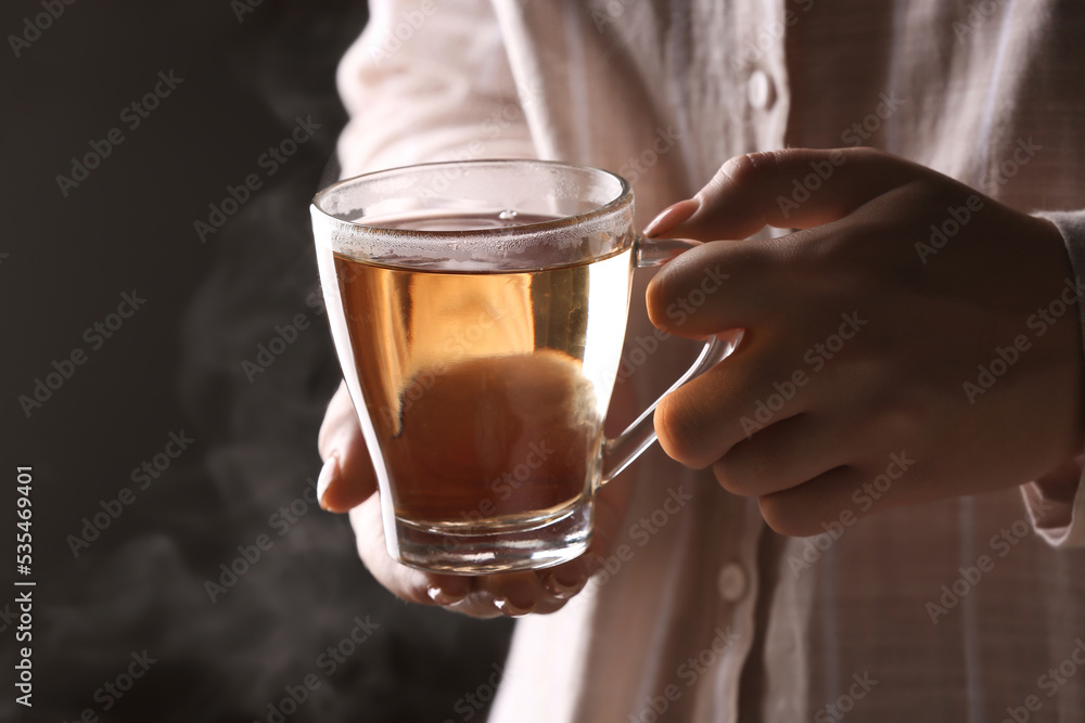 Woman holding glass cup of hot tea on black background, closeup