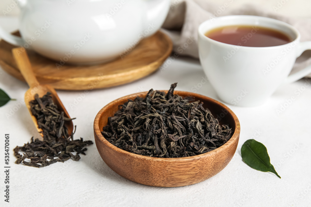 Bowl with dry tea leaves and cup of hot beverage on white background