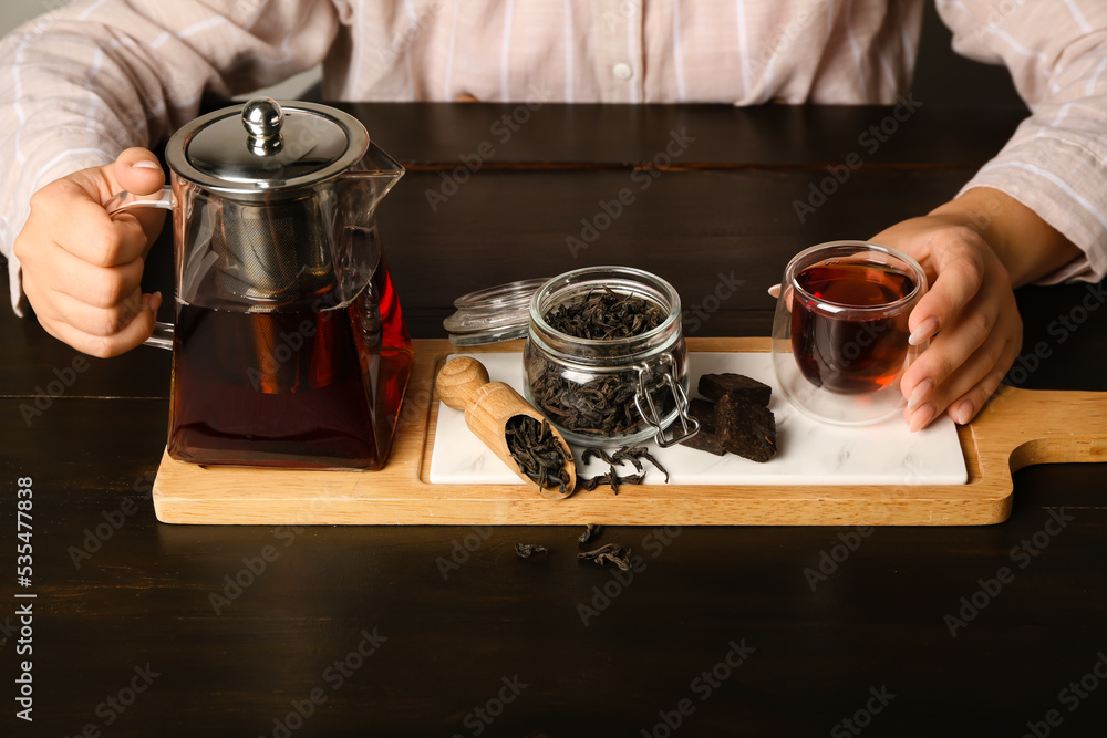 Woman with teapot, cup of puer tea and dry leaves sitting at dark wooden table