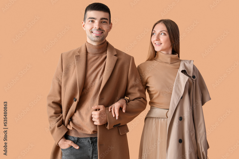 Fashionable young couple in autumn clothes on beige background