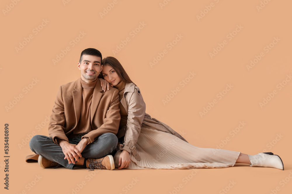 Fashionable young couple in autumn clothes on beige background