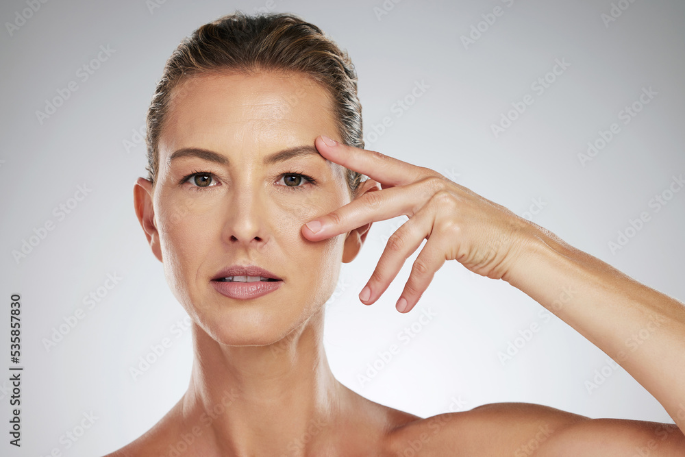 Face, beauty and eyes with a mature woman taking care of her eye or skin in studio on a gray backgro