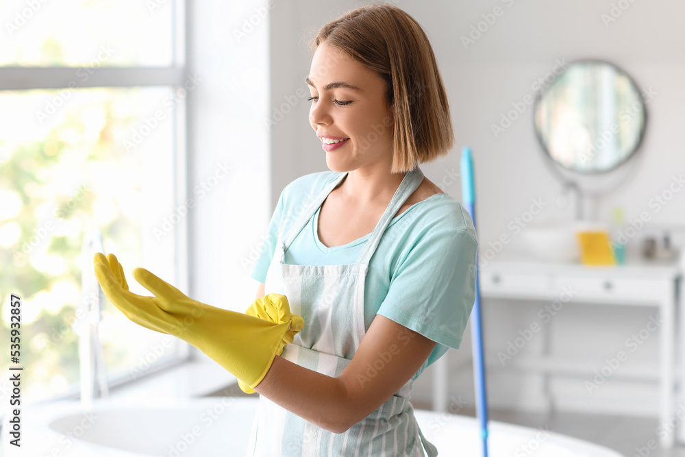 Young housewife putting on rubber glove in bathroom