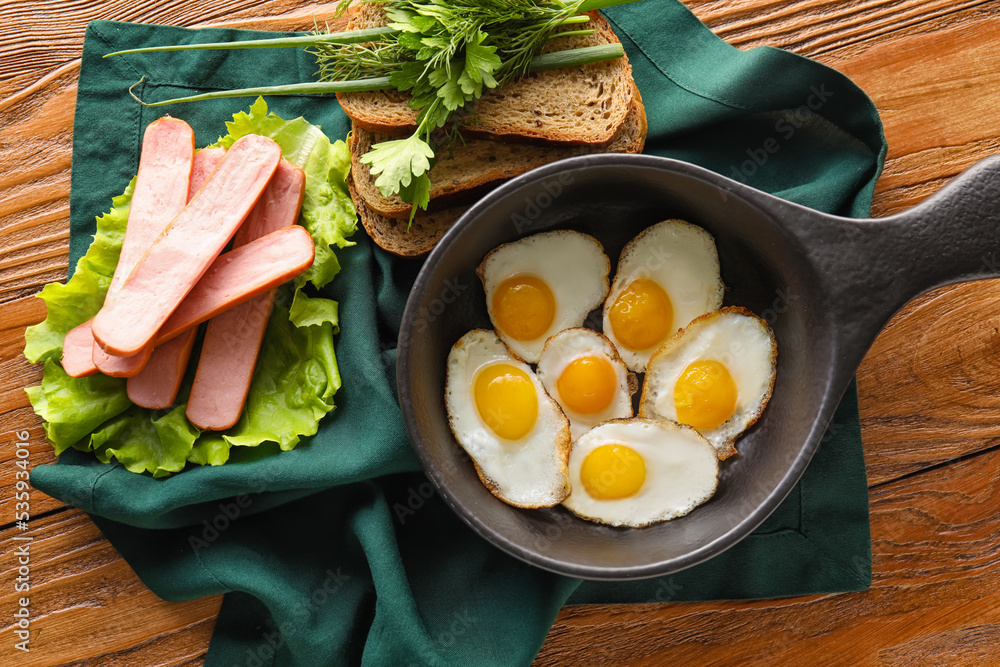 Composition with fried quail eggs, sausages and bread on wooden background