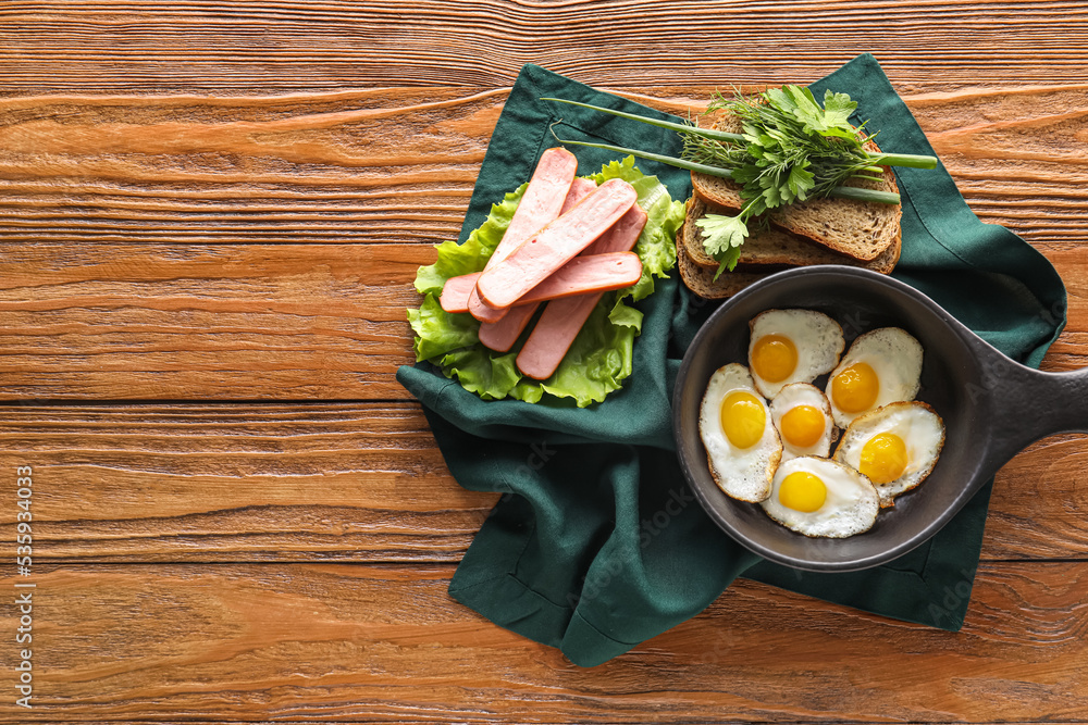 Composition with fried quail eggs, sausages and bread on wooden background