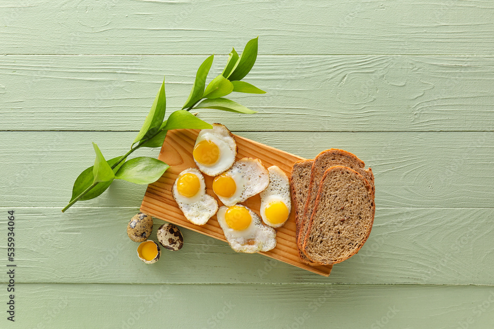 Board with tasty fried quail eggs and bread on color wooden background