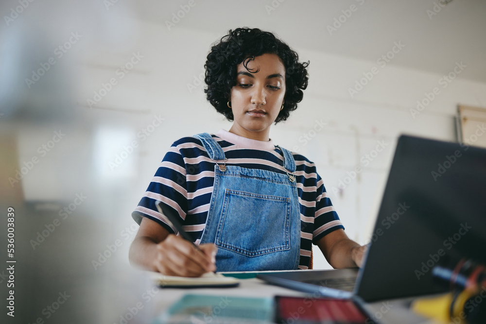 Black woman writing notes, studying on laptop and working on living room desk from home. African Ame