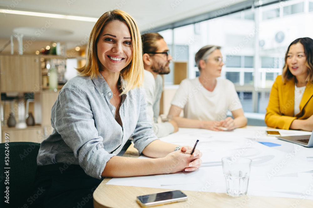 Happy young designer sitting in a meeting with her team