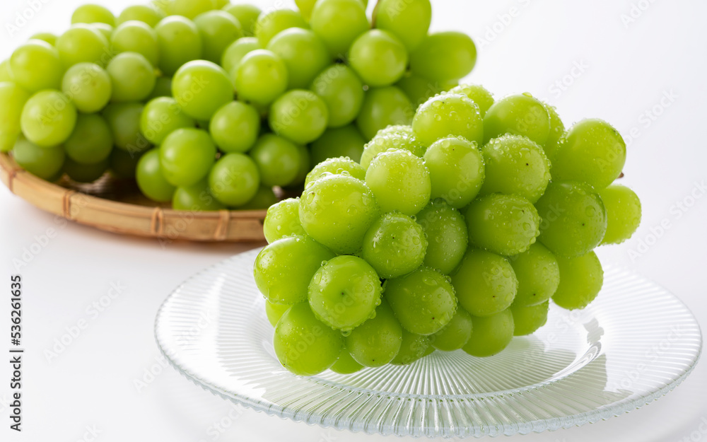 Shine Muscat with water droplets placed on glass plate with white background.