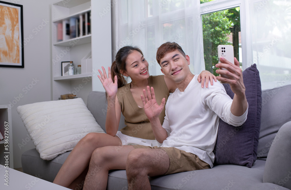 Happy young Asian couple taking selfie on sofa in the living room. Man and Woman couple lifestyle co