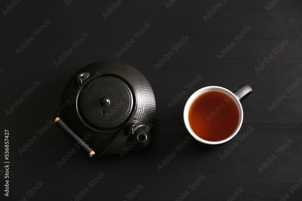 Tea pot and cup of hot beverage on black wooden background