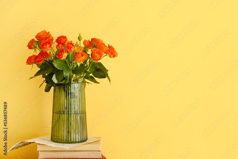 Vase with bouquet of beautiful roses with books on yellow background