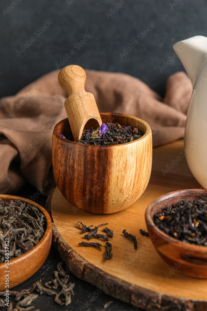 Bowls with dry tea leaves and scoop on dark table