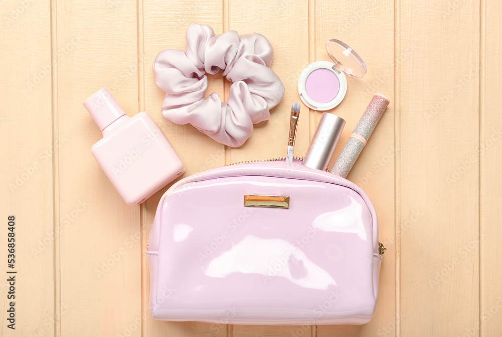 Cosmetic bag with different female accessories on color wooden background