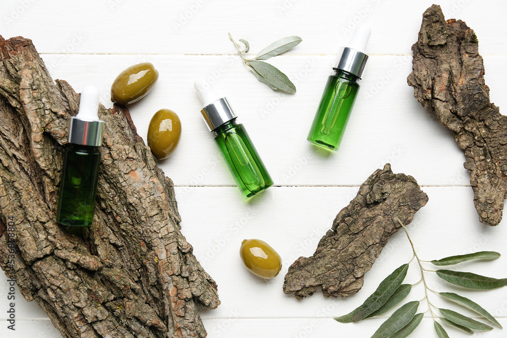 Composition with bottles of essential olive oil and tree bark on white wooden background