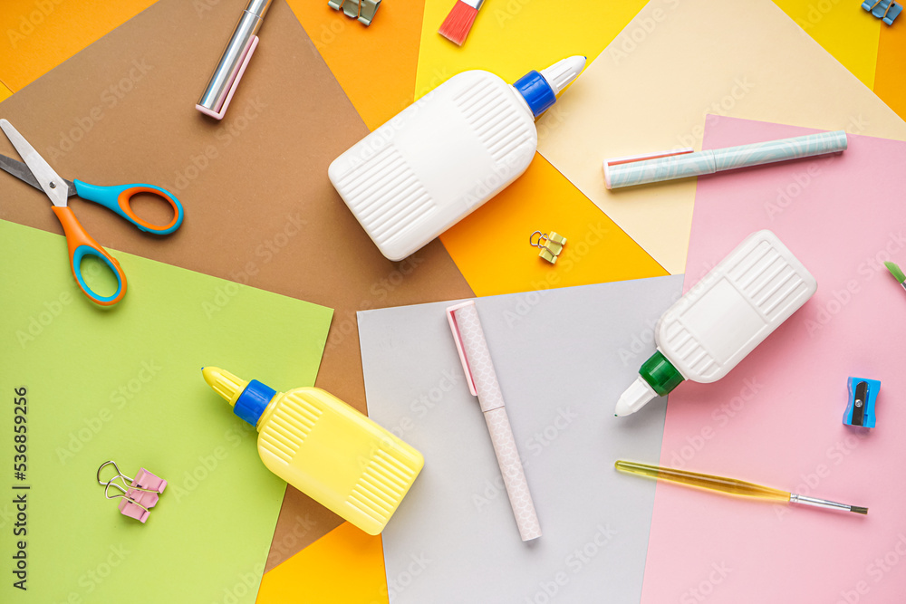 Bottles of glue with stationery and paper sheets on color background