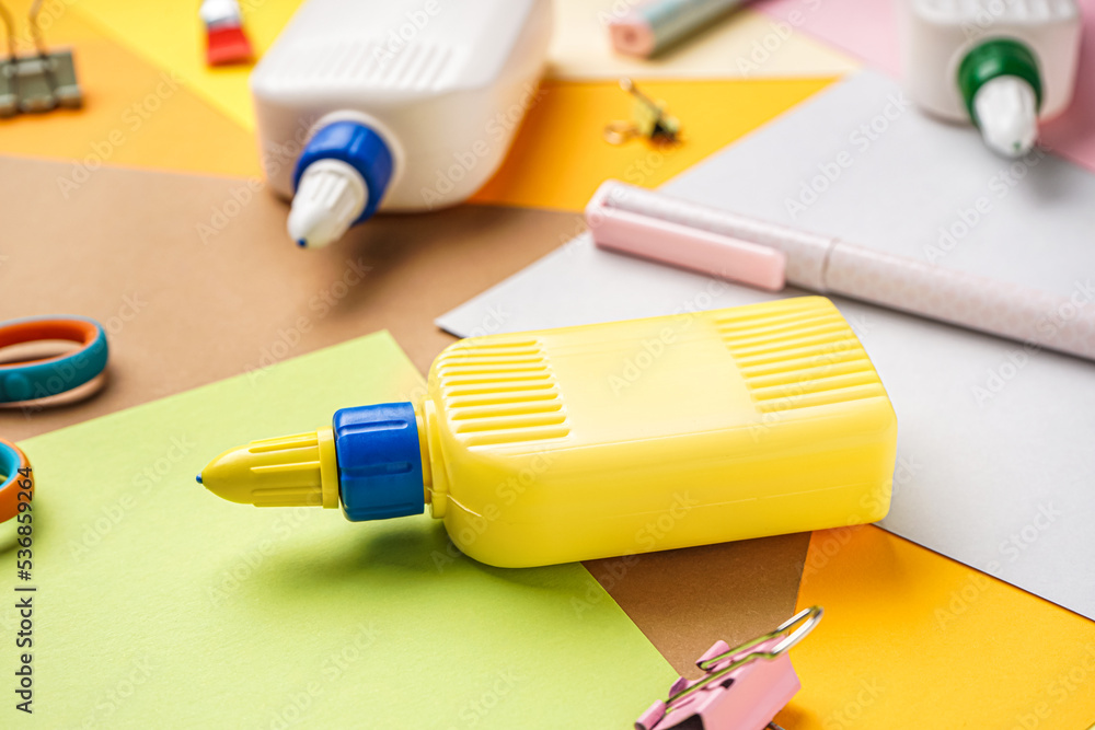 Bottle of glue with paper sheets on color background, closeup