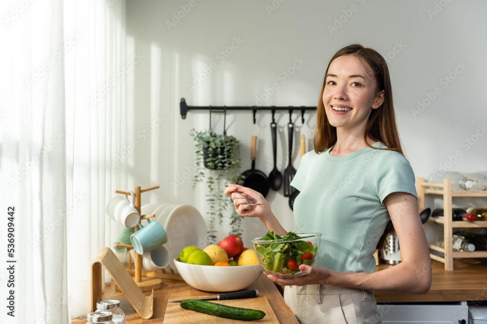 年轻的高加索女孩在家里的厨房里吃绿色沙拉的画像。