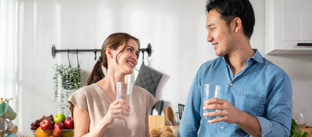 Asian attractive couple drinking a glass of water in kitchen at home. 