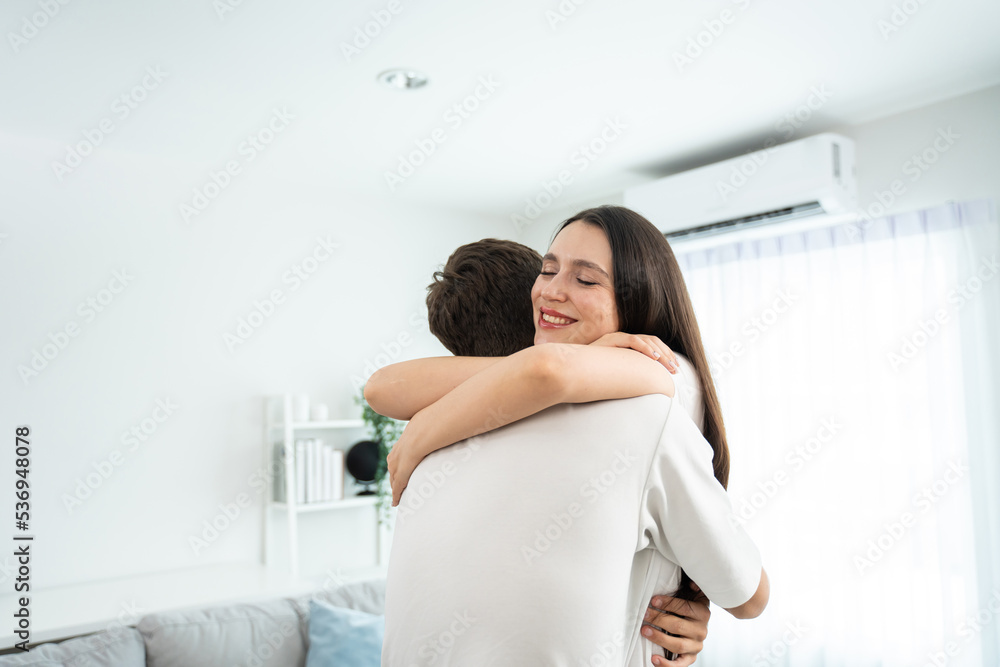 Caucasian young man and woman hugging each other in living room at home